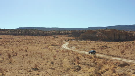 Aerial-of-4x4-car-driving-across-open-desert-landscape-on-dirt-road,-4K
