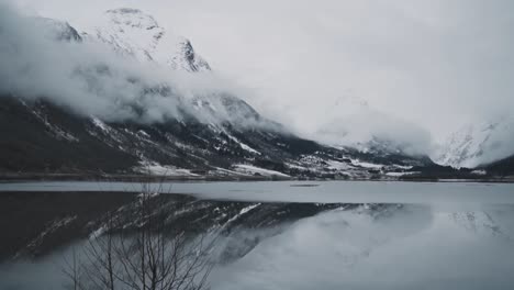 Fjord-mountain-covered-in-snow-and-cloud-layer-reflects-on-crystal-clear-Nordic-lake-water