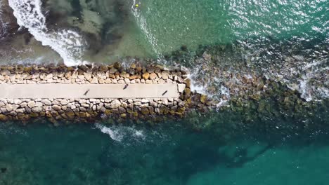 Old-ruined-pier-on-pebbly-beach-with-transparent-water