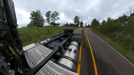 Rear-view-perspective-of-truck-driving-a-on-a-country-road-under-a-cloudy-sky-with-woods-on-both-sides