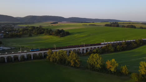 Luftaufnahme-Eines-Zugviadukts-Mit-Einem-Vorbeifahrenden-Zug-Und-Der-Umliegenden-Landschaft-Und-Stadt-Im-Hintergrund