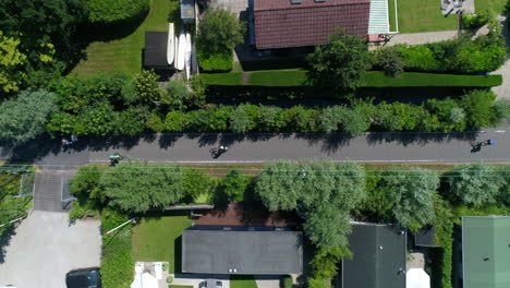 Aerial-View-Of-Bikers-Biking-In-The-Road-Along-Houses-In-The-Town-Near-Reeuwijkse-Plassen-In-Netherlands