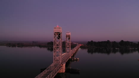 Drone-passes-over-vertical-lift-bridge-crossing-Sacramento-River-in-California-at-dusk
