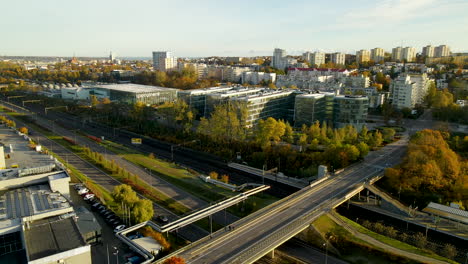 Railway-train-moving-on-wailroad-under-the-bridge-passing-Pomeranian-Science-and-Technology-Park-Gdynia-buildings-at-sunrise-in-Autumn---aerial-view