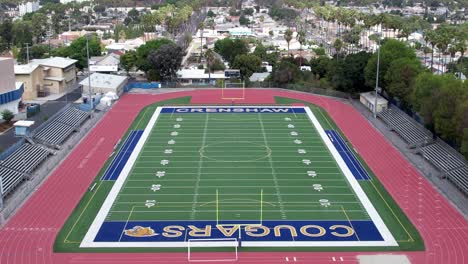 Crenshaw-Cougars-football-field-and-track,-rising-aerial-over-the-city,-empty-stadium