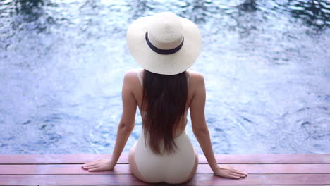 Rücken-Einer-Frau-In-Badeanzug-Und-Sommerlichem-Floppy-Sonnenhut,-Die-Auf-Einem-Spa-Schwimmbadrand-Mit-Sprudelndem-Wasser-Sitzt,-Hochwinkelansicht,-Urlaubsvorlage-In-Zeitlupe