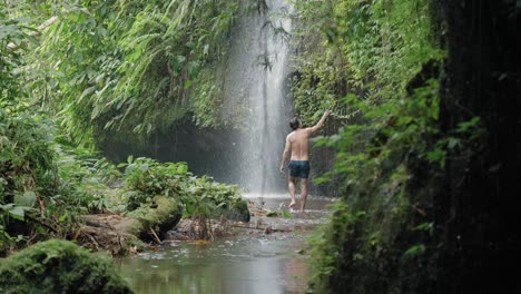 Man-walking-in-front-of-waterfall-in-rainforest