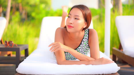 Portrait-of-Red-haired-Young-Thai-Woman-Resting-Lying-on-Belly-on-Deckchair-leaning-on-elbows-smiling-and-in-Hotel-Lounge-in-Florida,-USA---static-slow-motion