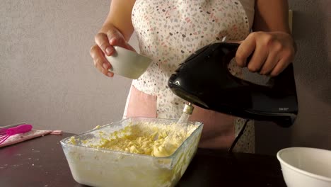 Mujer-Latina-Usando-Un-Delantal-Preparando-Cocinar-Horneando-Un-Pastel-Vertiendo-Leche-En-La-Masa-Y-Mezclando
