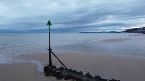 Coastal-tide-marker-aerial-view-low-orbit-right-across-moody-overcast-low-tide-seaside-beach