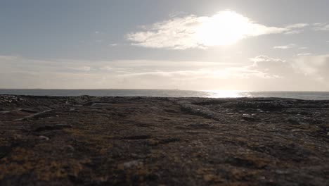 Ocean-horizon-splits-frame,-rocky-beach-foreground,-distant-lighthouse