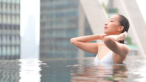 Close-up-of-a-sexy-woman-in-a-rooftop-resort-swimming-pool-pushing-wet-hair-away-from-her-face