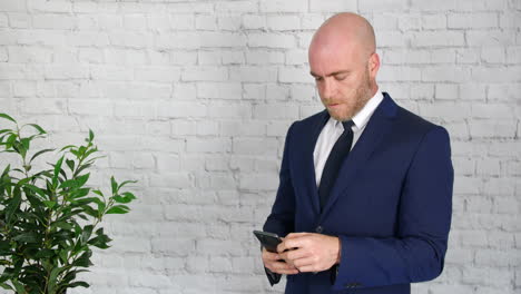 A-businessman-in-a-suit-with-a-beard-texting-and-browsing-on-his-phone-while-on-a-break-at-work