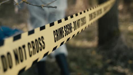 Crime-scene-do-not-cross-yellow-tape-hanging-between-trees,-photographer-in-background
