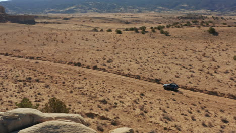 Panning-with-car-driving-down-rural-dirt-road-through-desert-landscape