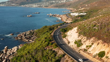Car-Driving-Through-Victoria-Road-At-Sunset-In-Oudekraal,-South-Africa