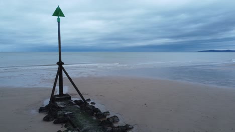 Coastal-tide-marker-aerial-view-low-reverse-reveal-across-moody-overcast-low-tide-seaside-beach