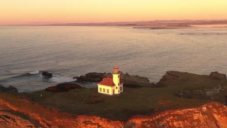 Cape-Arago-Lighthouse-illuminated-by-setting-sun,-Oregon-Coast-4k-drone