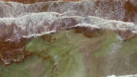 Aerial-Drone-Top-Down-View-Of-Waves-Breaking-On-Beach-Shore-With-Orange-Brown-Seaweed-In-Water