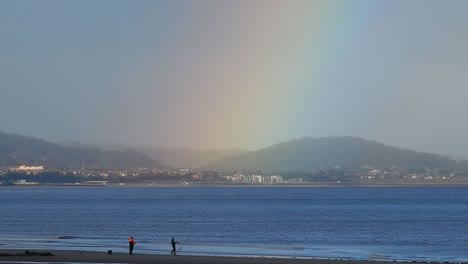 Men-fishing-under-scenic-rainbow-beautiful-colours-over-Welsh-mountains-coastal-seascape-horizon