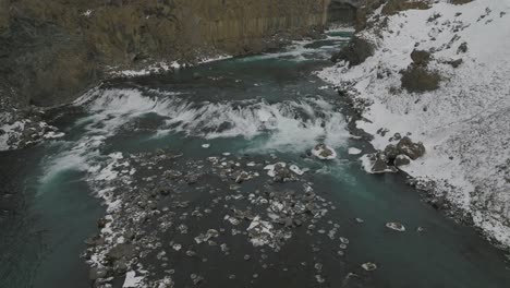Río-Que-Fluye-Escénico-Por-La-Cascada-De-Aldeyjarfoss-En-El-Paisaje-Nevado-De-Islandia---Antena