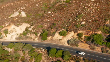 Aerial-View-Of-White-Car-Traveling-Along-The-Victoria-Road-In-Oudekraal,-South-Africa