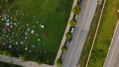 Aerial-view-above-a-crowd-sitting-on-lawn-at-a-concert-in-Louisville,-USA---rotating,-tilt,-drone-shot