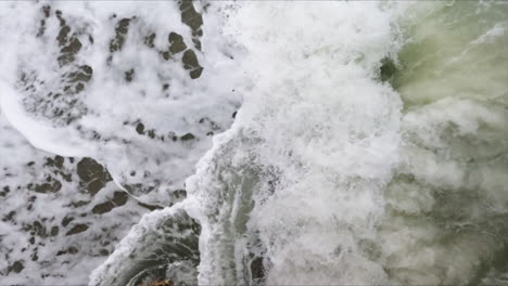 Super-slow-motion-shot-of-a-white-foam-ocean-wave-hitting-a-large-dark-rock-in-the-sea