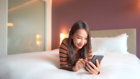 Woman-lying-down-on-the-bed-and-using-social-media-on-phone---touch-and-scrolling-on-a-smartphone-screen-smiling