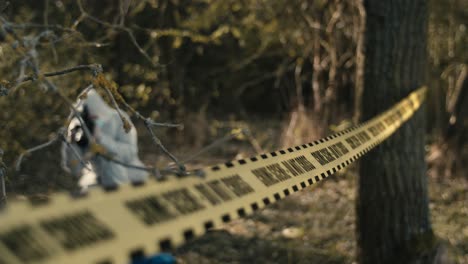 Crime-scene-investigation-outdoor,-yellow-tape-hanging-between-trees,-csi-photographer-in-background