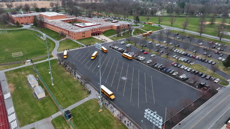Aerial-of-American-school-campus-with-yellow-school-bus-arrival-and-departure