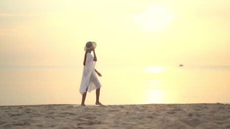 An-attractive-woman-in-a-loose-fitting-cover-up-walks-along-the-beach-at-sunset