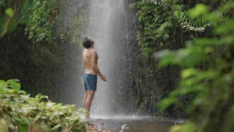 Attractive-man-standing-in-front-of-waterfall-in-rainforest