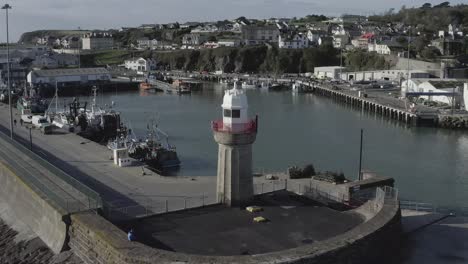 Retreating-aerial-of-lighthouse-at-fishing-harbour-in-Irish-coast-town