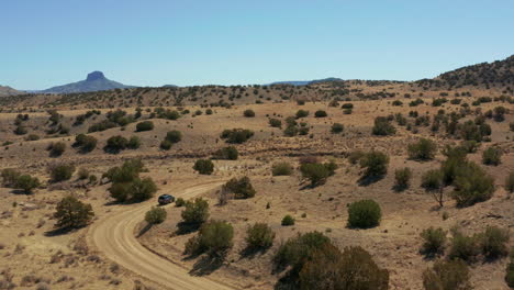 Aerial-following-car-down-curvy-dirt-road-in-desert-landscape