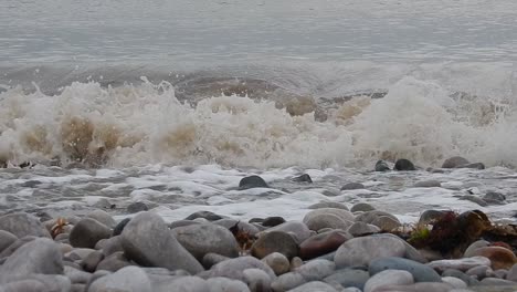Foaming-white-waves-washing-into-calming-serene-rocky-pebble-stone-shoreline
