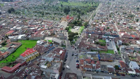Drone-aerial-footage-of-urban-colonial-city-park-Parque-El-Calvario-in-Central-American-highlands-city-Quetzaltenango,-Xela,-Guatemala-with-traffic-driving-around-on-a-sunny-day