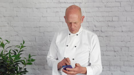 A-male-head-chef-is-raking-a-break-from-the-kitchen-and-is-texting-and-browsing-the-internet-on-his-phone