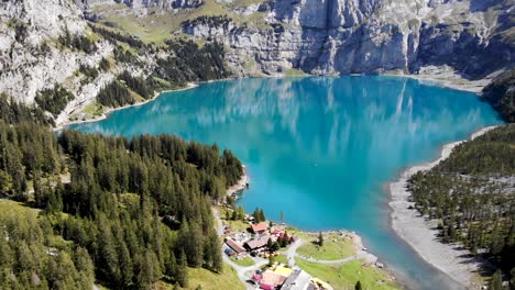 Aerial-flyover-next-to-lake-Oeschinensee-in-Kandersteg,-Switzerland-with-a-reflection-of-the-cliffs-of-Bluemlisalphorn-on-the-turquoise-water