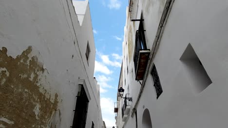 POV-looking-up-while-walking-through-narrow-streets-of-city-with-blue-sky