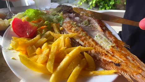 Eating-a-grilled-sea-bass-with-french-fries-and-a-salad,-traditional-spanish-food-in-a-restaurant,-4K-shot