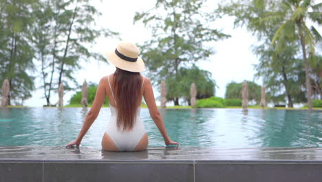 Back-View-of-Lonely-Slender-Young-Woman-at-Poolside-of-Luxury-Hotel-Resort-at-Tropical-Destination