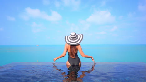 Infinity-Pool,-Classy-Female-in-Swimsuit-and-Endless-Blue-Tropical-Sea-Horizon