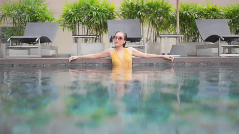Fresh-from-a-swim-a-strong-attractive-woman-leans-along-the-wall-of-a-resort-swimming-pool
