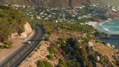 Luftaufnahme-Von-Autos,-Die-Auf-Der-Victoria-Road-Mit-Häusern-Am-Wasser-In-Oudekraal,-Südafrika,-Fahren