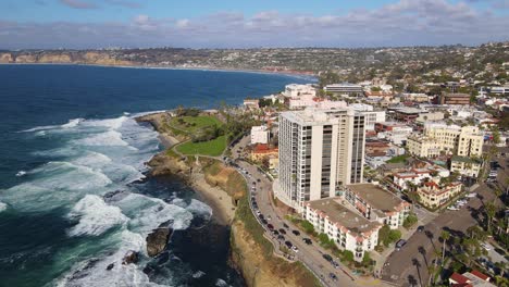 Aerial-Panoramic-around-a-high-rise-apartment-building-by-the-coast-with-small-waves-rolling-up-on-shore-with-beach-houses-in-the-background