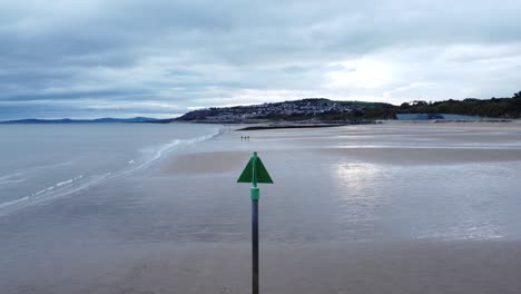 Coastal-tide-marker-aerial-view-low-descending-pull-back-across-moody-overcast-low-tide-seaside-beach