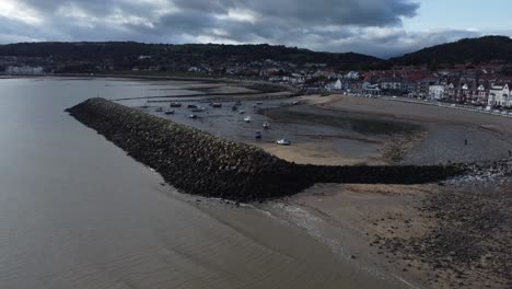 North-Wales-seaside-town-coastline-hotels-harbour-breakwater-aerial-view-low-tide-orbit-left