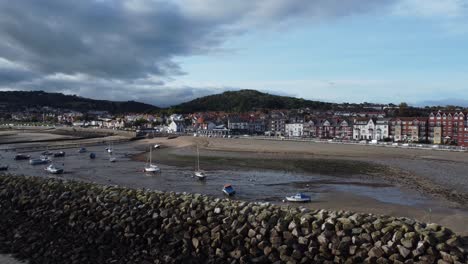 North-Wales-seaside-town-coastline-hotels-harbour-breakwater-aerial-view-low-right-orbit