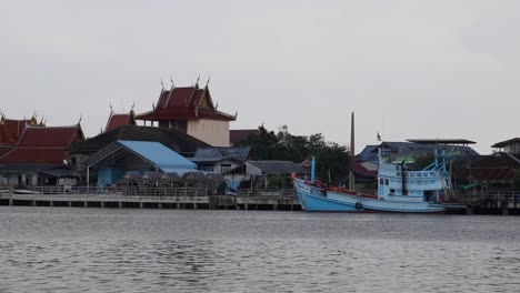 4k-ansicht-Eines-Tempels-Und-Eines-Holzbootes,-Die-Entlang-Des-Flusses-Von-Bang-Tabun,-Thailand,-Verankert-Sind